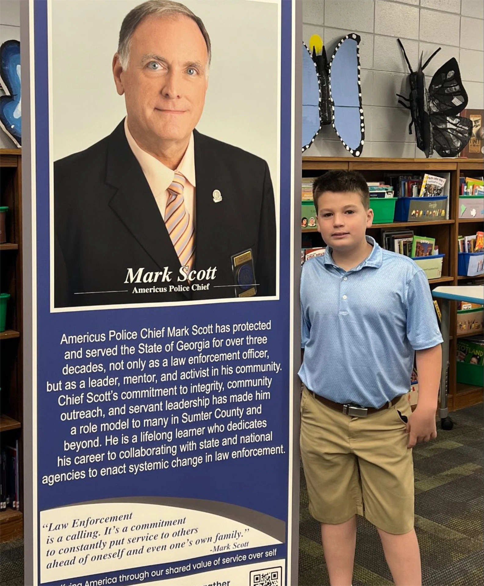Middle school student standing by banner stand for Americus Police Chief Mark Scott at Furlow Charter School's Museum for Service