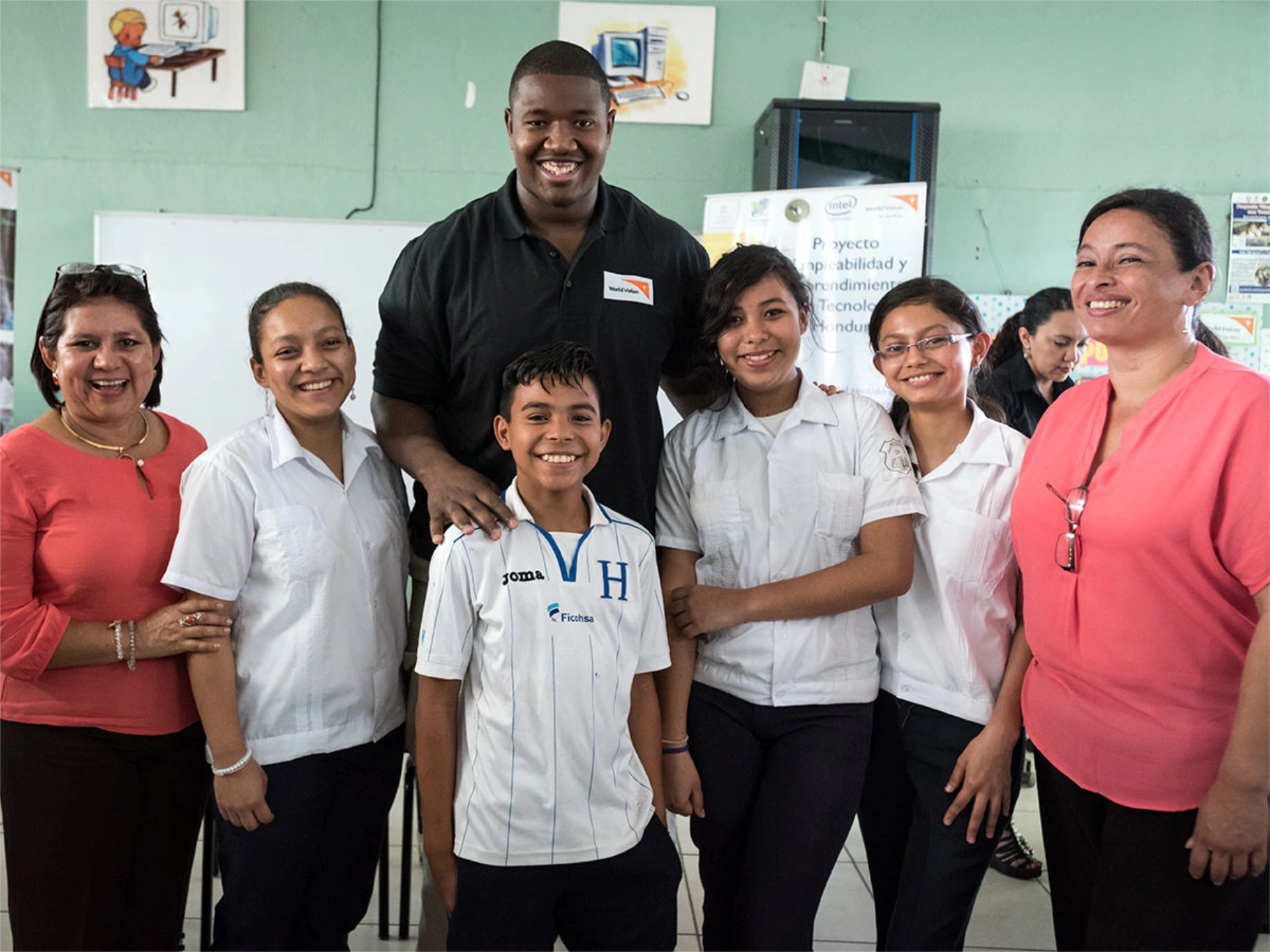 Kelvin smiling in a group photo with students and teachers