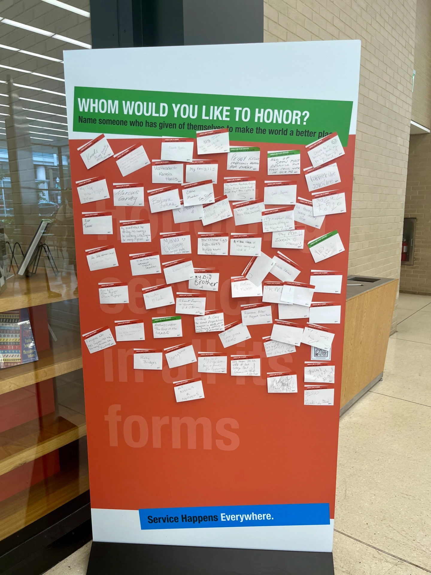 Large display sign with text "Whom would you like to honor?" with space underneath filled with sticky notes with handwritten notes