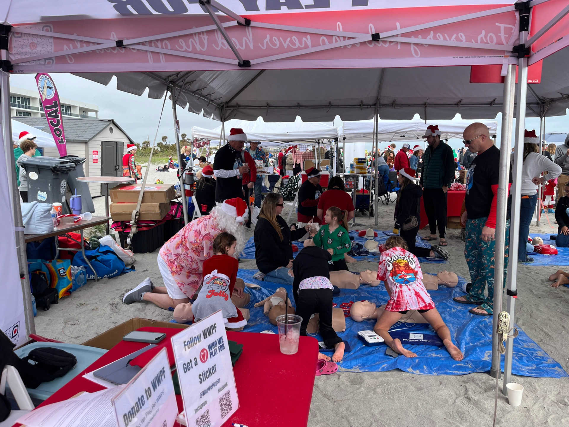 People under tent at Who We Play For event on beach completing CPR training