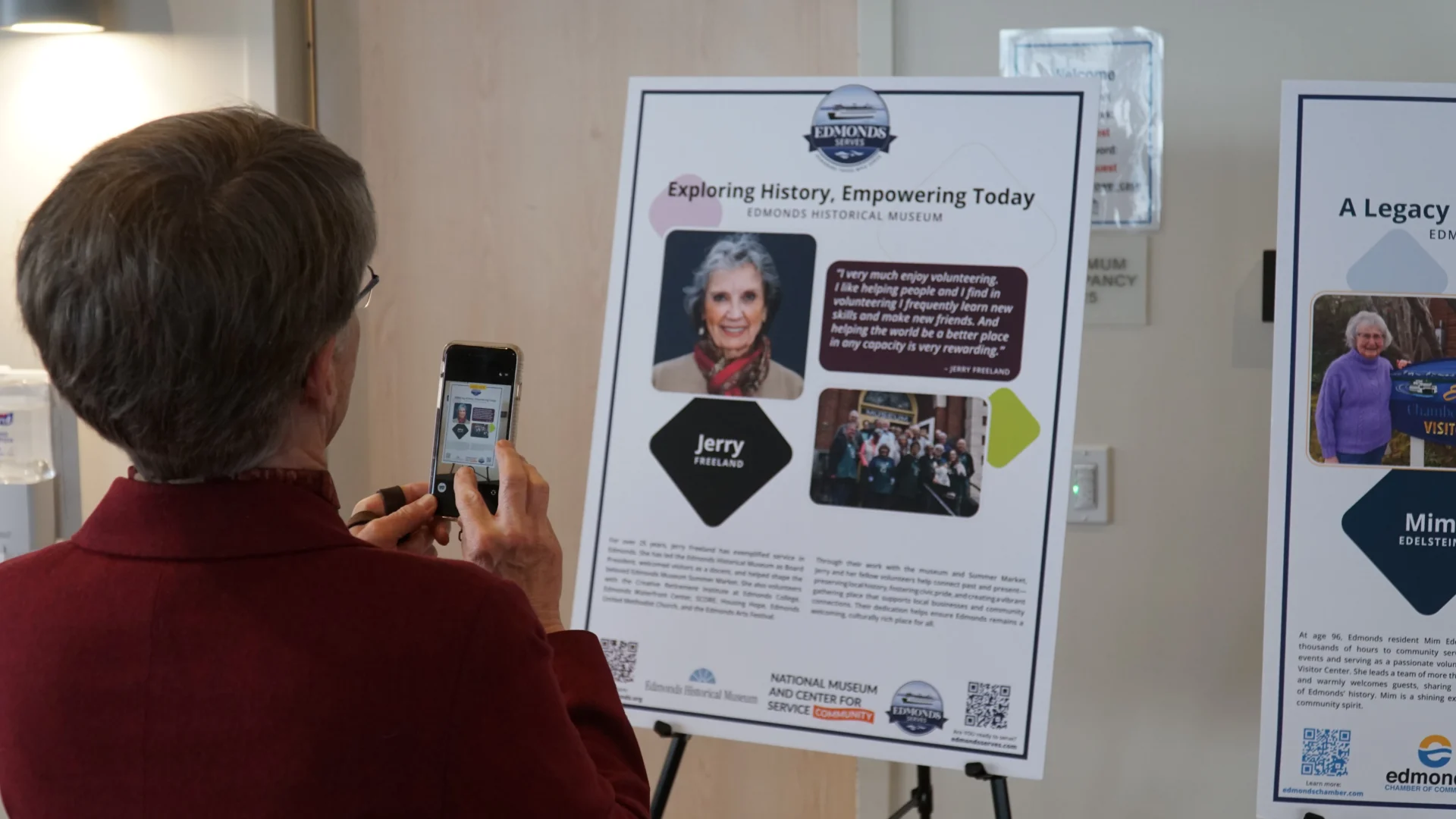 Woman taking a photo with her phone of a display, telling a story about someone who serves in Edmonds. 