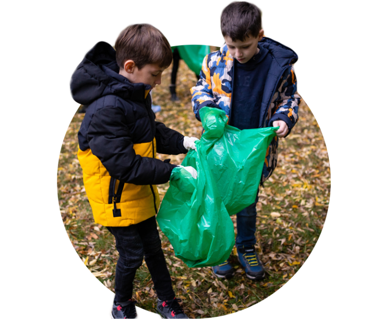 Two children collecting garbage at park, with their heads extending outside the circle frame