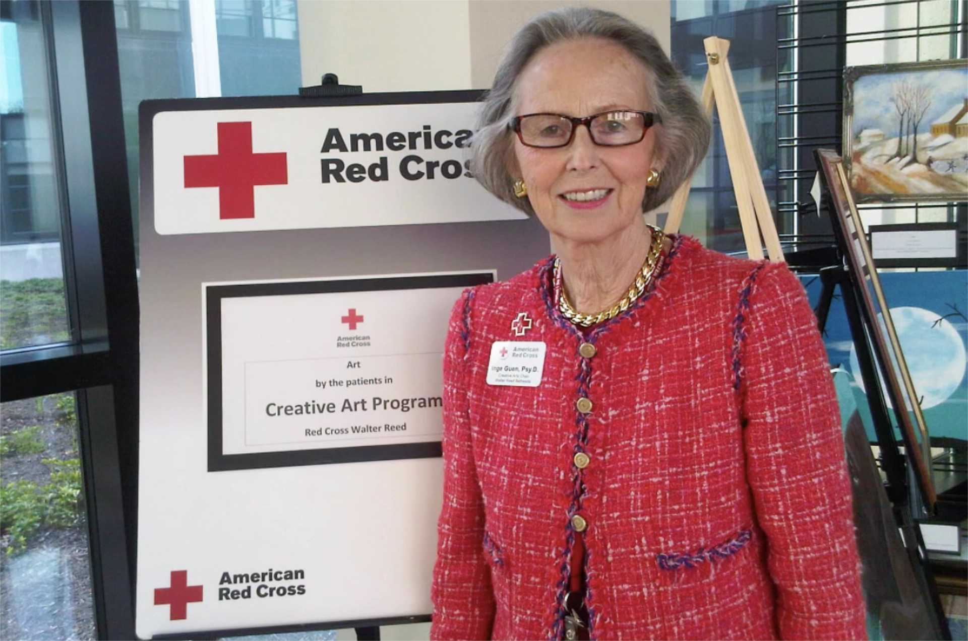 Dr. Inge Guen posing with sign for Creative Art Program award from the American Red Cross at Walter Reed National Military Medical Center
