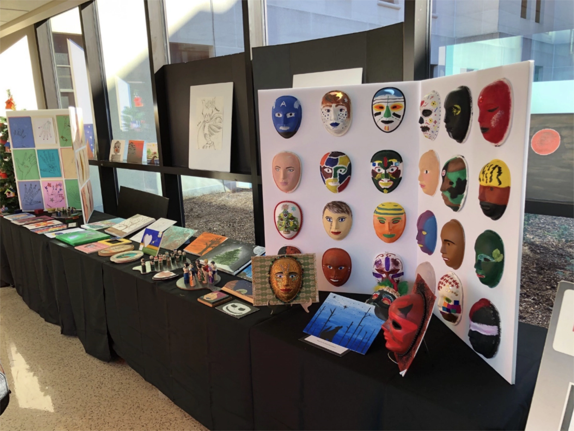 Tables with displays of artwork made by Dr. Guen's patients, showing illustrations, sculptures, and colorful masks