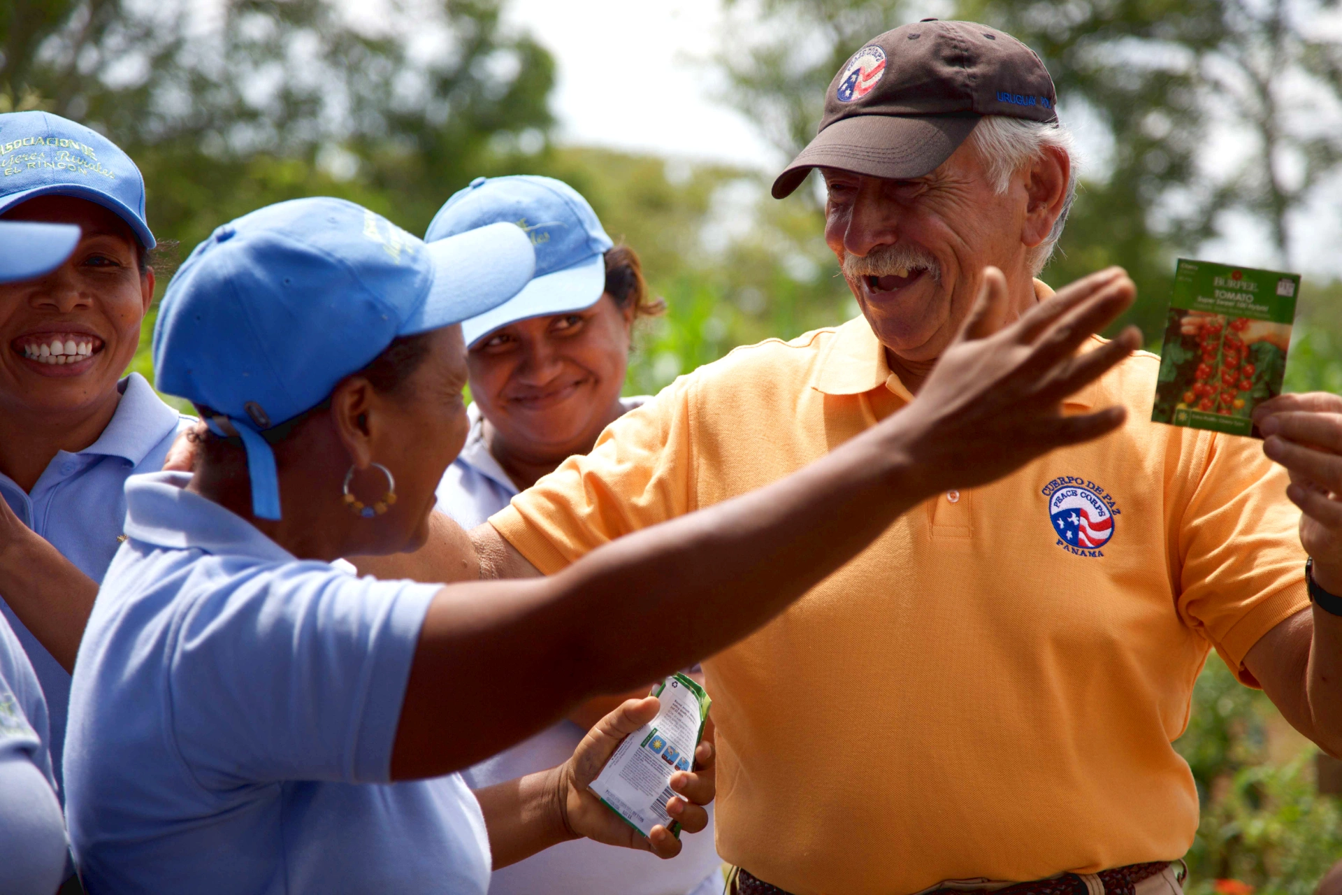 Man in Peace Corps smiling and about to hug woman in another organization while holding seed packets