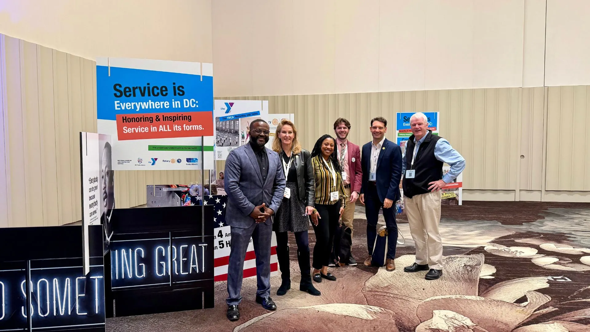 A group of 6 people standing next to the Service is Everywhere in DC exhibit at the ISNS 2025